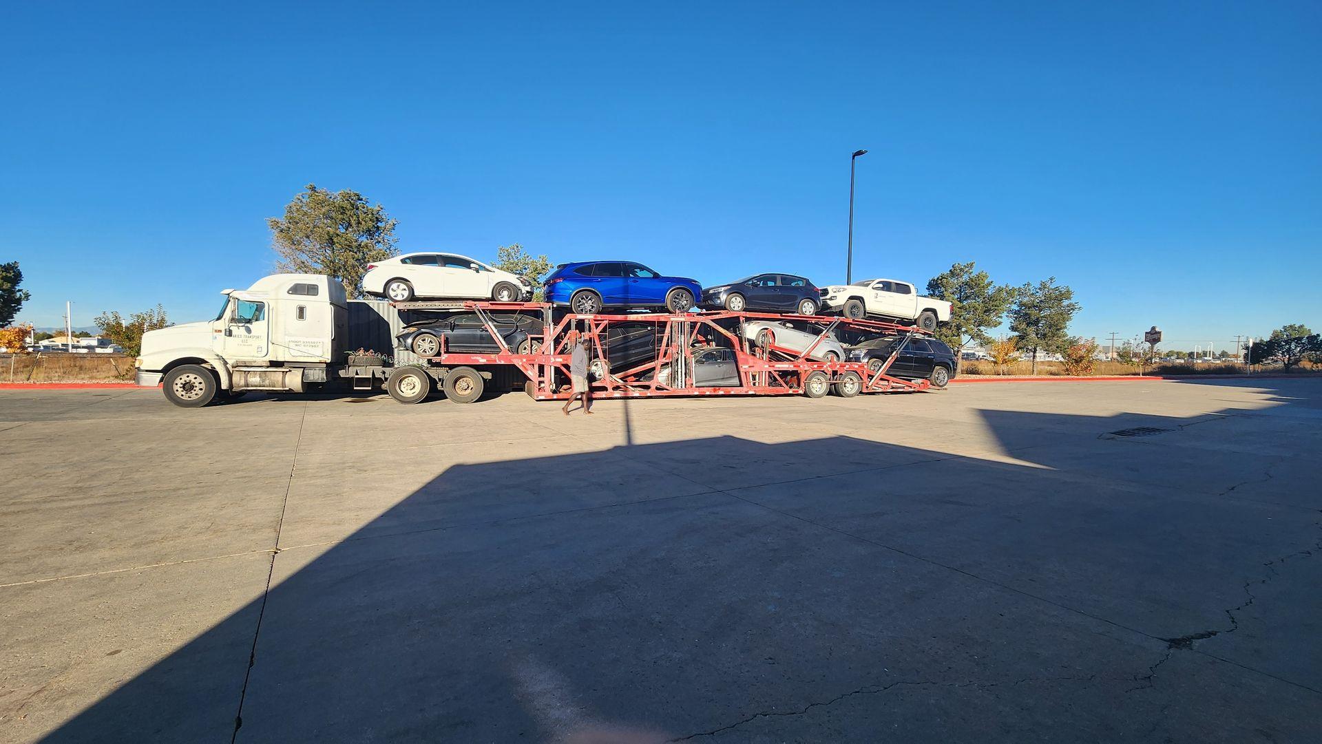 A truck carrying multiple cars on a transport trailer parked in an open lot on a clear day.