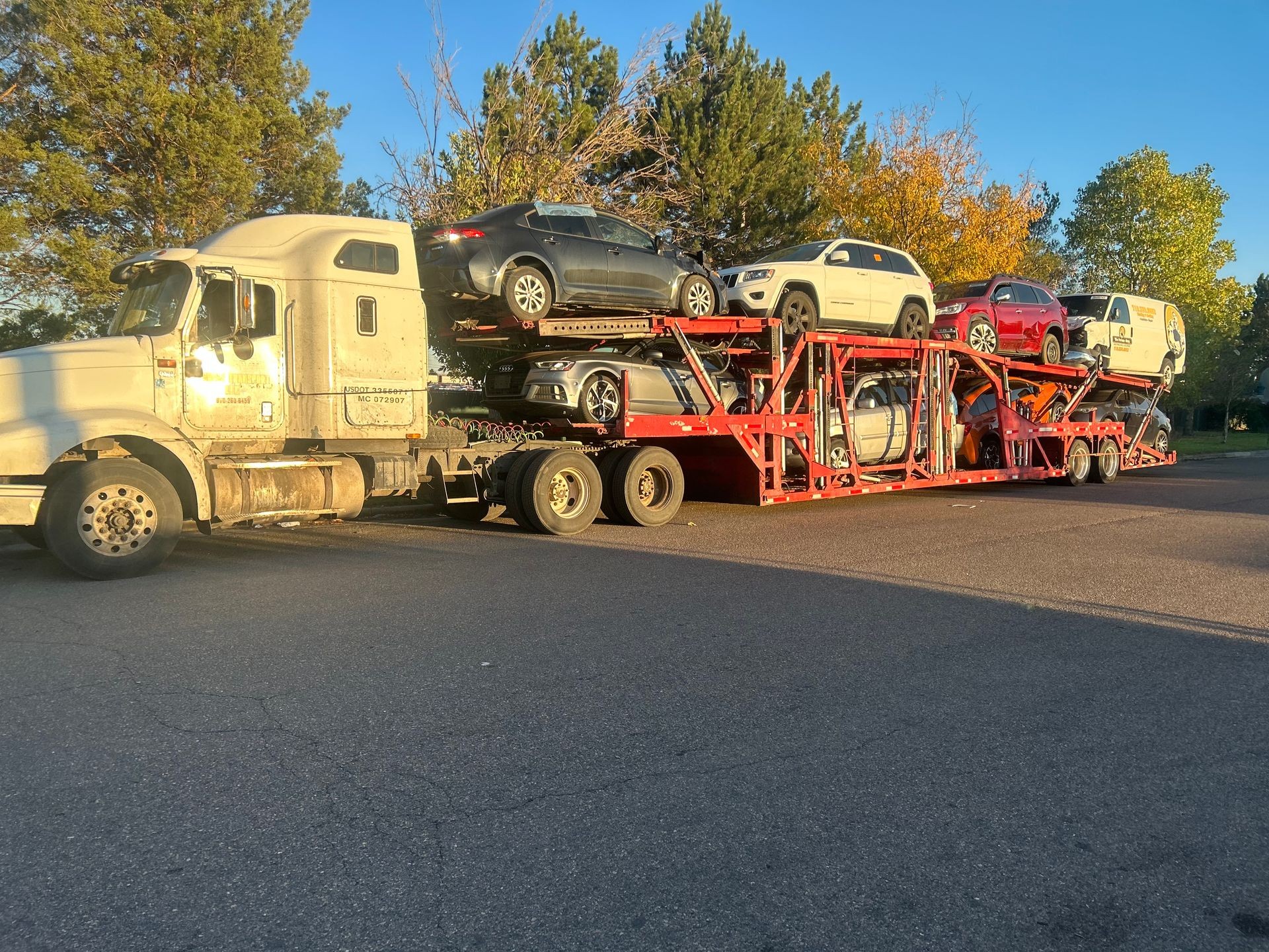 A car carrier truck transporting multiple vehicles on a clear day with trees in the background.