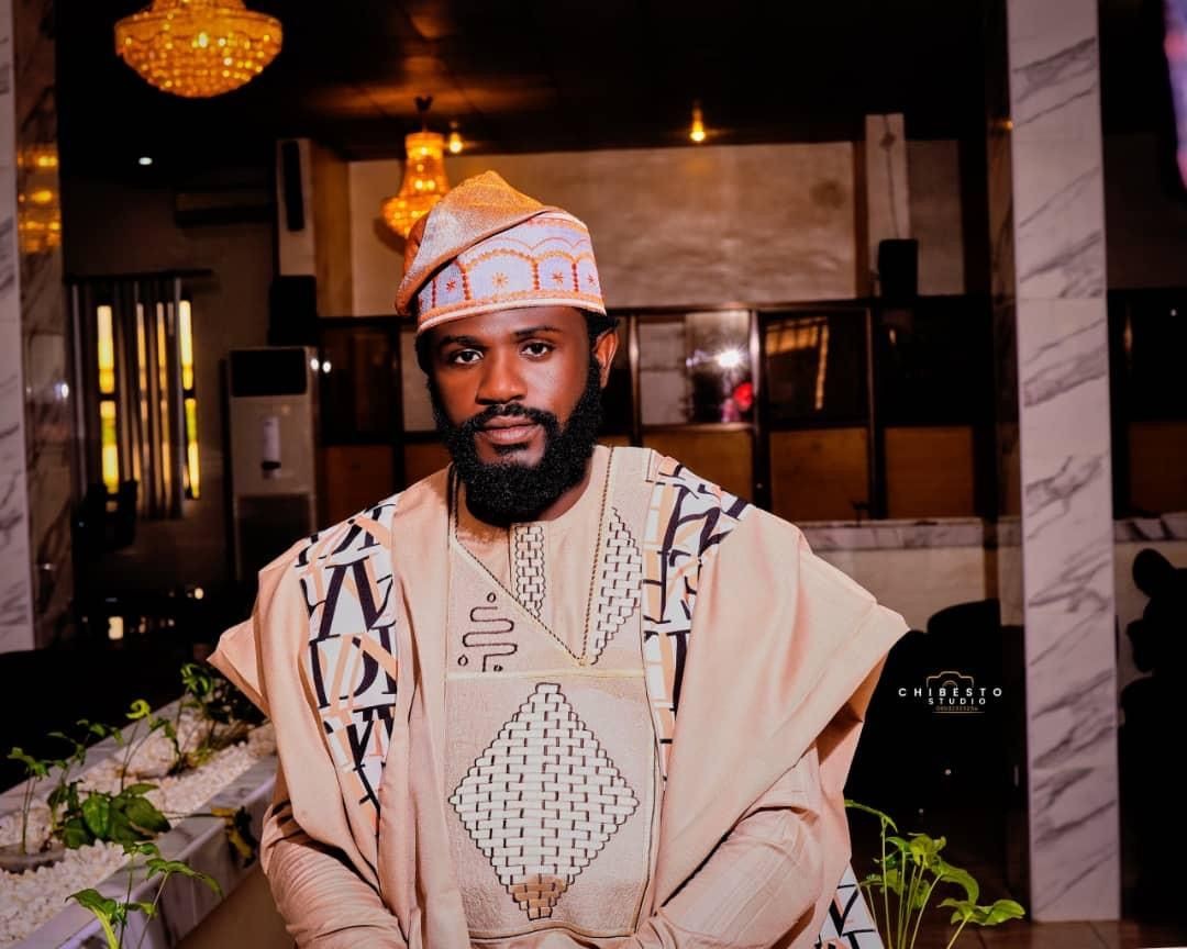 Person wearing traditional African attire with ornate patterns in a room with chandeliers and marble columns.